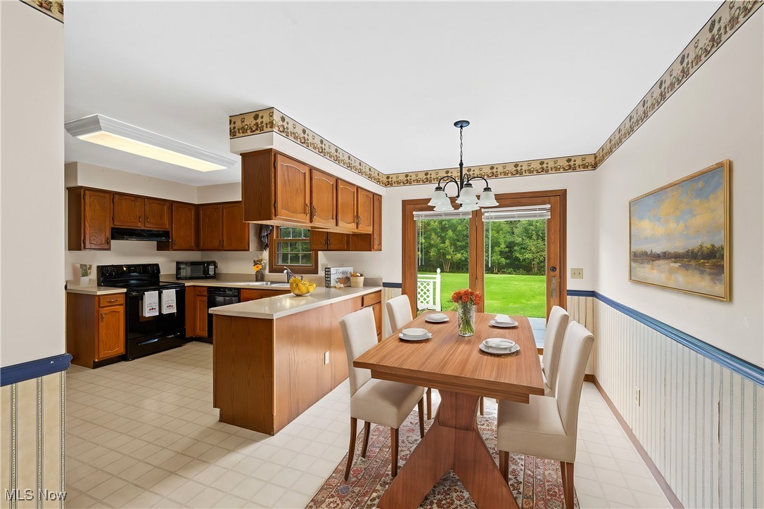 Kitchen featuring pendant lighting, sink, kitchen peninsula, an inviting chandelier, and black appliances