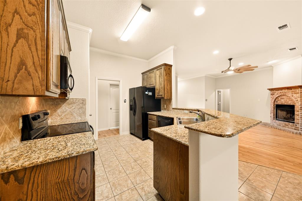 2105 Ridgewood Drive Bridgeport, TX 76426 - Photo 11 of 27 Kitchen featuring granite countertops, wood cabinetry, tile flooring, and black appliances, with a brick fireplace and wood flooring visible in the background