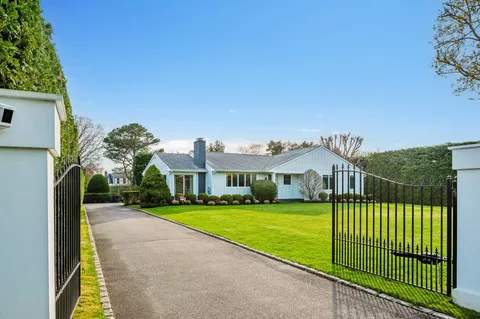 a view of a white house with a big yard plants and large trees