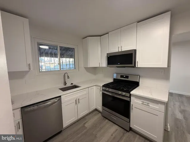 a kitchen with white cabinets appliances a sink and a window