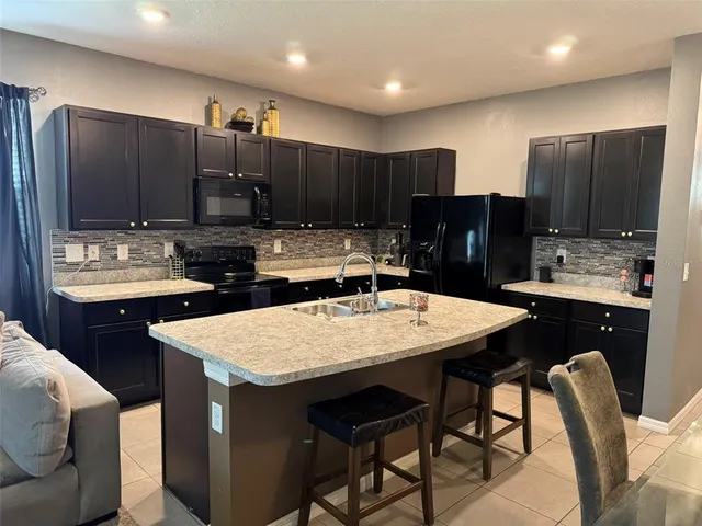 a kitchen with stainless steel appliances kitchen island granite countertop a table chairs sink refrigerator and cabinets