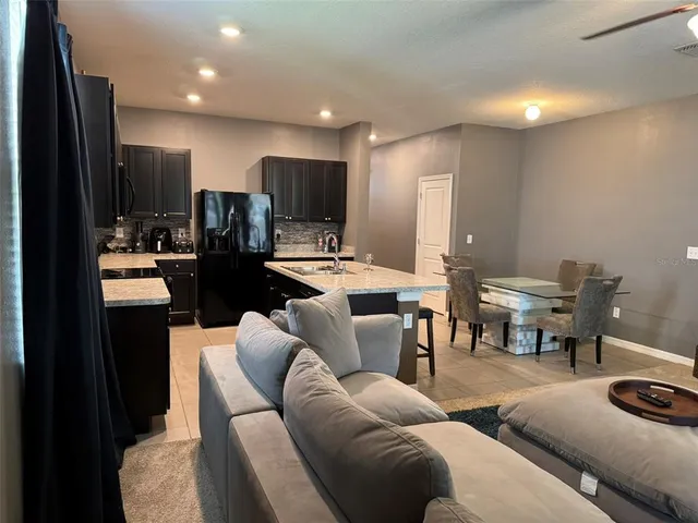 a living room with furniture kitchen area and a refrigerator