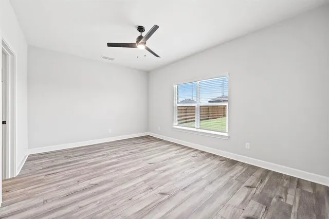 an empty room with wooden floor fan and windows