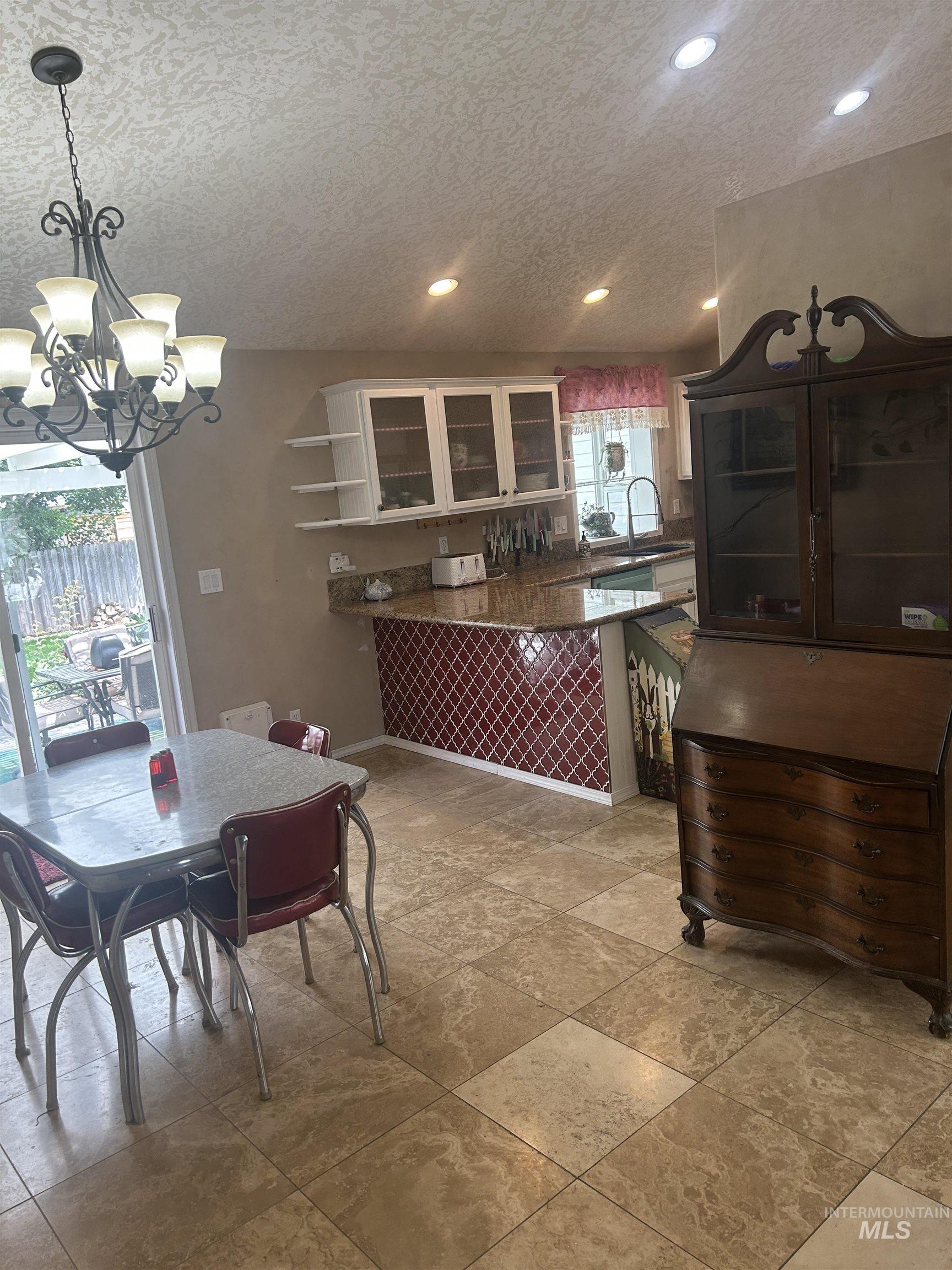 1444 East Doberman Street Meridian, ID 83642 - Photo 9 of 31 Kitchen and dining area featuring large format tile flooring, a kitchen island with a granite-style countertop, white cabinetry with glass inserts, recessed lighting, and a sliding glass door to the exterior