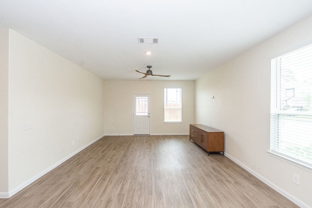 23502 Glenbuck St Spring Spring, TX 77373 - Photo 12 of 50 This spacious room features light-colored walls and wood flooring, creating a cozy atmosphere. It includes a ceiling fan, a large window for natural light, a door leading outside, and a modern cabinet, perfect for a versatile living area.