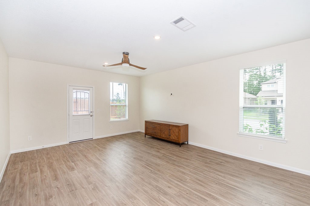23502 Glenbuck St Spring Spring, TX 77373 - Photo 13 of 50 Spacious, light-filled living area with wood flooring, neutral walls, and a modern ceiling fan. Large windows and a door to the outside enhance natural light. Suitable for various furniture arrangements.