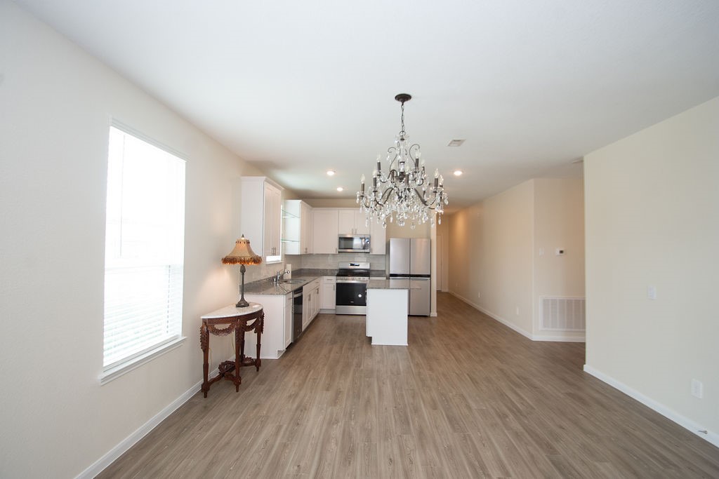 23502 Glenbuck St Spring Spring, TX 77373 - Photo 17 of 50 This photo showcases a bright, open-concept kitchen and dining area. It features modern stainless steel appliances, white cabinetry, and a stylish chandelier. The space is complemented by wood flooring and ample natural light from a large window.