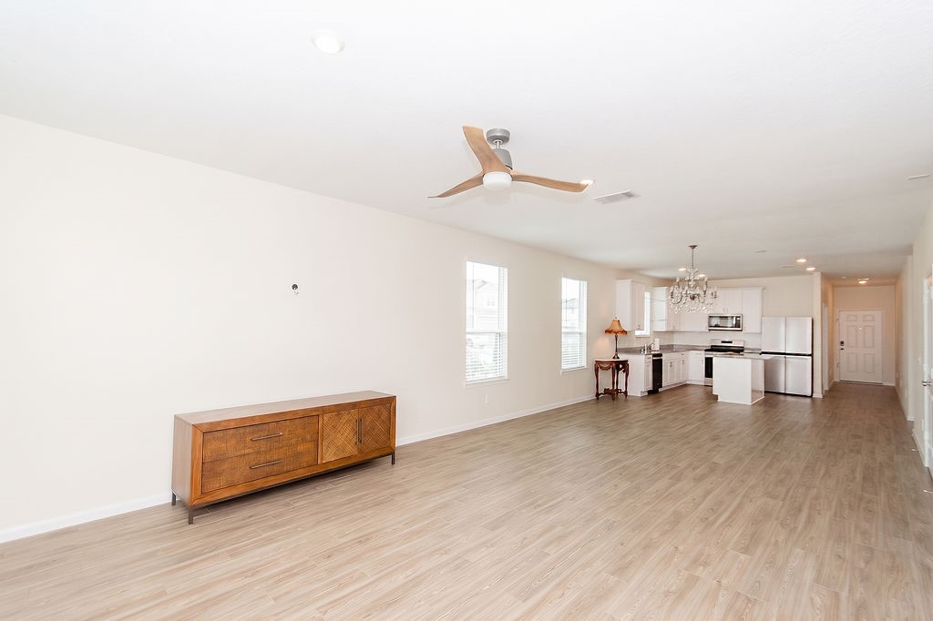 23502 Glenbuck St Spring Spring, TX 77373 - Photo 19 of 50 This spacious open-concept living area features wood flooring, a ceiling fan, and abundant natural light. The modern kitchen boasts stainless steel appliances and a stylish chandelier, perfect for entertaining or family gatherings.