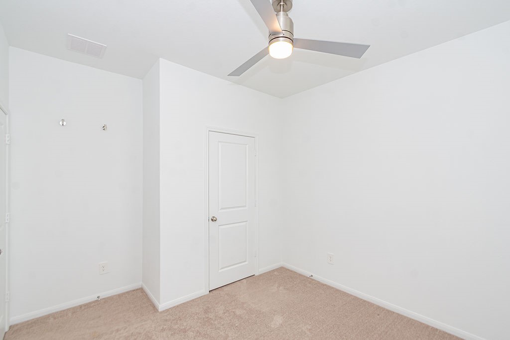 23502 Glenbuck St Spring Spring, TX 77373 - Photo 21 of 50 This room features a clean, minimalist design with neutral walls and carpet, a ceiling fan with light, and a standard door, offering a blank canvas for personalization.