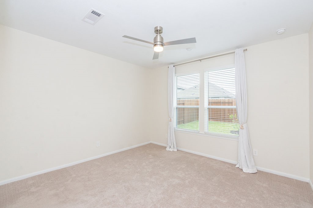 23502 Glenbuck St Spring Spring, TX 77373 - Photo 24 of 50 This bright, neutral-toned room features a modern ceiling fan, plush carpet, and a large window with white curtains, offering plenty of natural light and a view of the backyard.