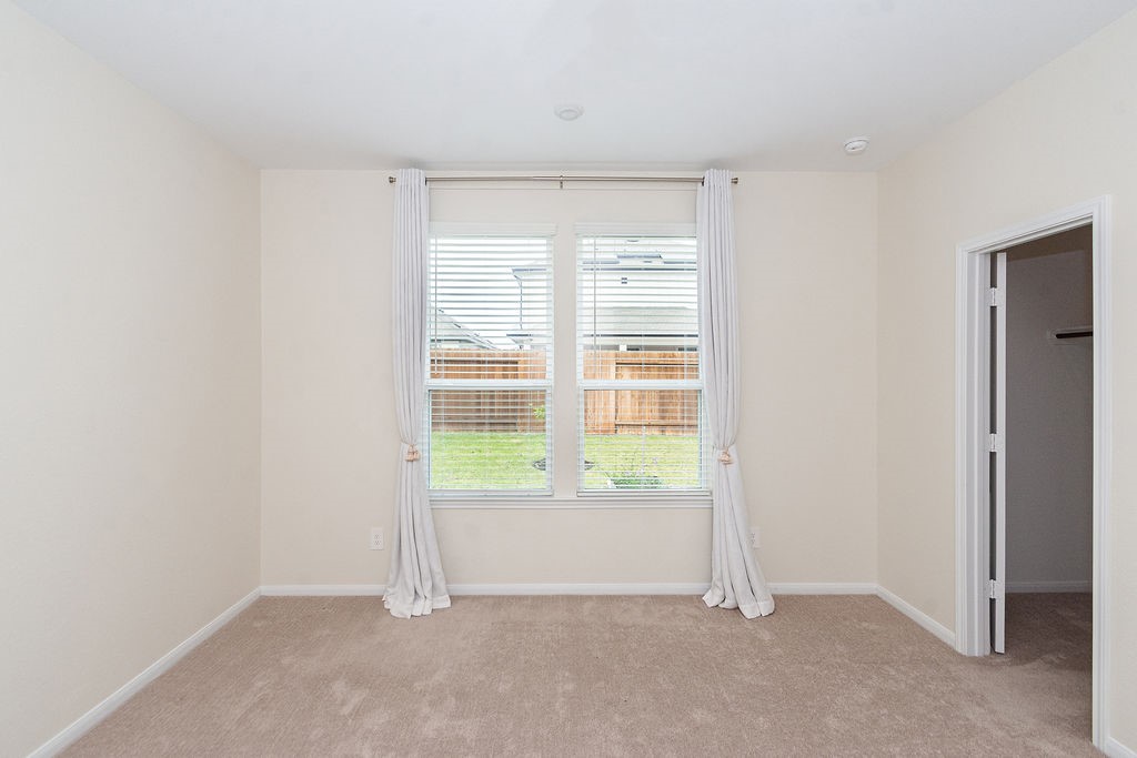 23502 Glenbuck St Spring Spring, TX 77373 - Photo 26 of 50 This room features neutral-colored walls and carpet, a large window with white curtains providing natural light, and an adjacent doorway leading to a walk-in closet, offering a bright and inviting space.
