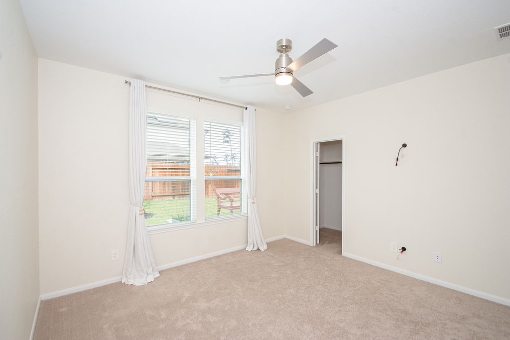 23502 Glenbuck St Spring Spring, TX 77373 - Photo 27 of 50 This room features neutral walls, a ceiling fan, and large windows with white curtains that provide natural light. It has carpeted floors and a small closet, offering a cozy and functional space.
