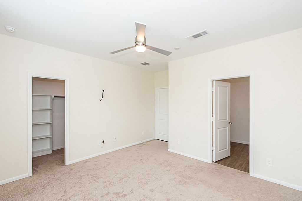 23502 Glenbuck St Spring Spring, TX 77373 - Photo 28 of 50 This photo showcases a spacious, neutral-colored bedroom with carpeted flooring, a ceiling fan, and ample natural light. It features two doorways, one leading to a closet with built-in shelving, and the other to an adjacent room.