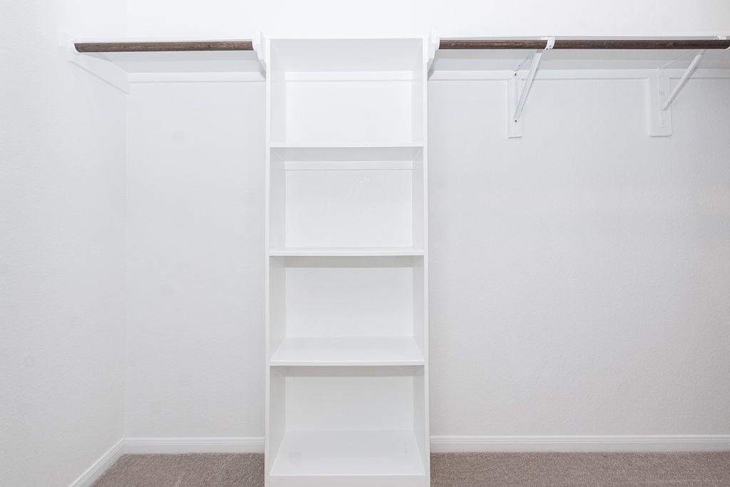 23502 Glenbuck St Spring Spring, TX 77373 - Photo 30 of 50 This is a spacious walk-in closet with white shelving in the center and hanging rods on both sides, offering ample storage and organization options.
