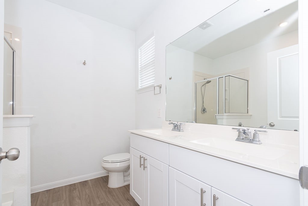 23502 Glenbuck St Spring Spring, TX 77373 - Photo 33 of 50 This bright bathroom features a large mirror, dual sinks with modern fixtures, a spacious shower, and stylish wood-look flooring, offering a clean and contemporary feel.