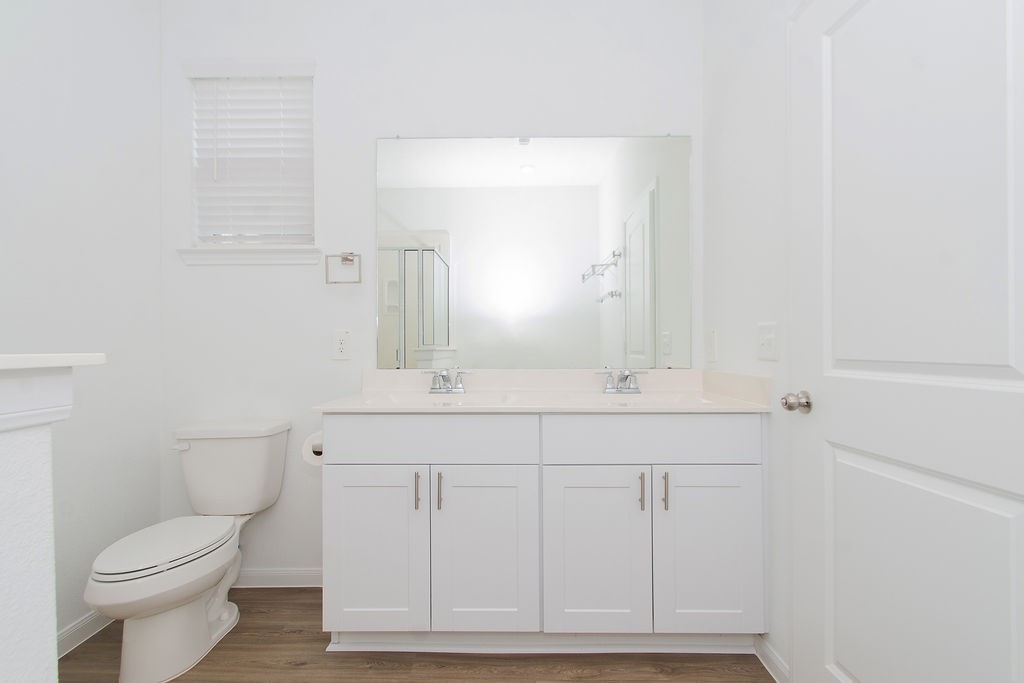 23502 Glenbuck St Spring Spring, TX 77373 - Photo 34 of 50 Bright and modern bathroom featuring a white vanity with dual sinks, a large mirror, and sleek cabinetry. The space is complemented by a toilet and wooden flooring, creating a clean and contemporary feel.