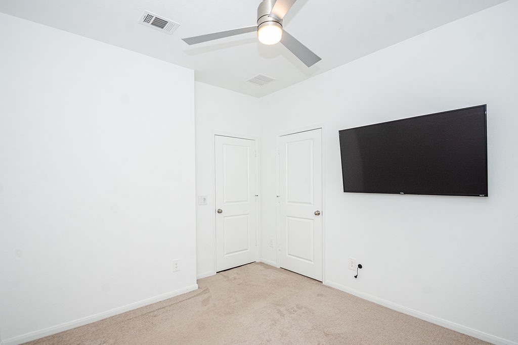 23502 Glenbuck St Spring Spring, TX 77373 - Photo 39 of 50 This room features a clean, modern design with white walls and a neutral carpet. It includes a ceiling fan and a wall-mounted TV, along with two doors, likely for a closet and entry. Perfect for a minimalist setup.