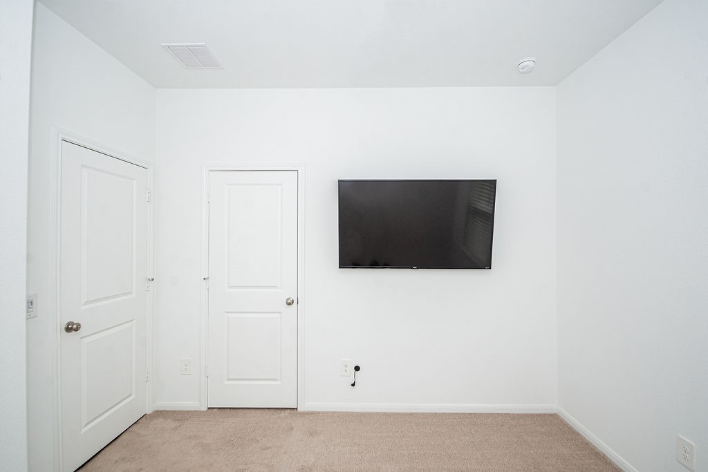 23502 Glenbuck St Spring Spring, TX 77373 - Photo 40 of 50 This room features clean, white walls with a mounted flat-screen TV. It has two closed doors and carpeted flooring, suggesting a cozy and modern space.