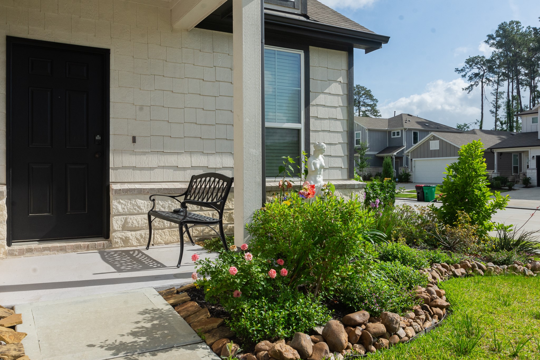 23502 Glenbuck St Spring Spring, TX 77373 - Photo 4 of 50 Charming front entry with a black door, cozy bench, and a well-maintained garden. The landscaped area features vibrant flowers and a small statue, offering a welcoming and picturesque view.