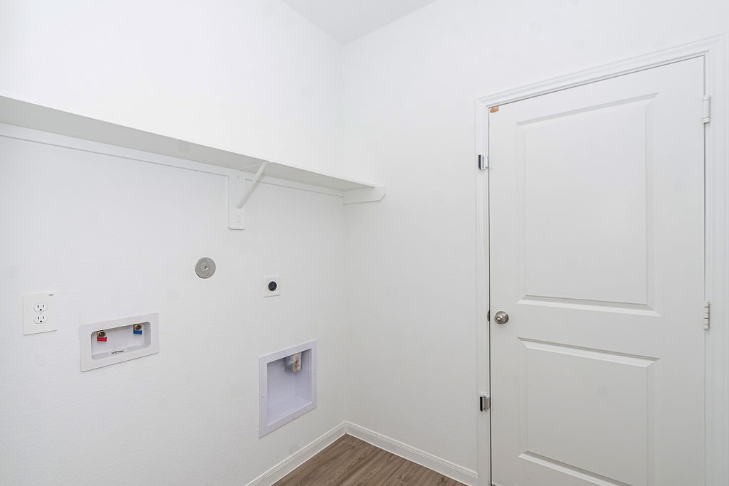 23502 Glenbuck St Spring Spring, TX 77373 - Photo 45 of 50 This photo shows a laundry room with hookups for a washer and dryer, a shelf for storage, and a door leading to another area. The walls and door are white, and the floor is a light wood finish.