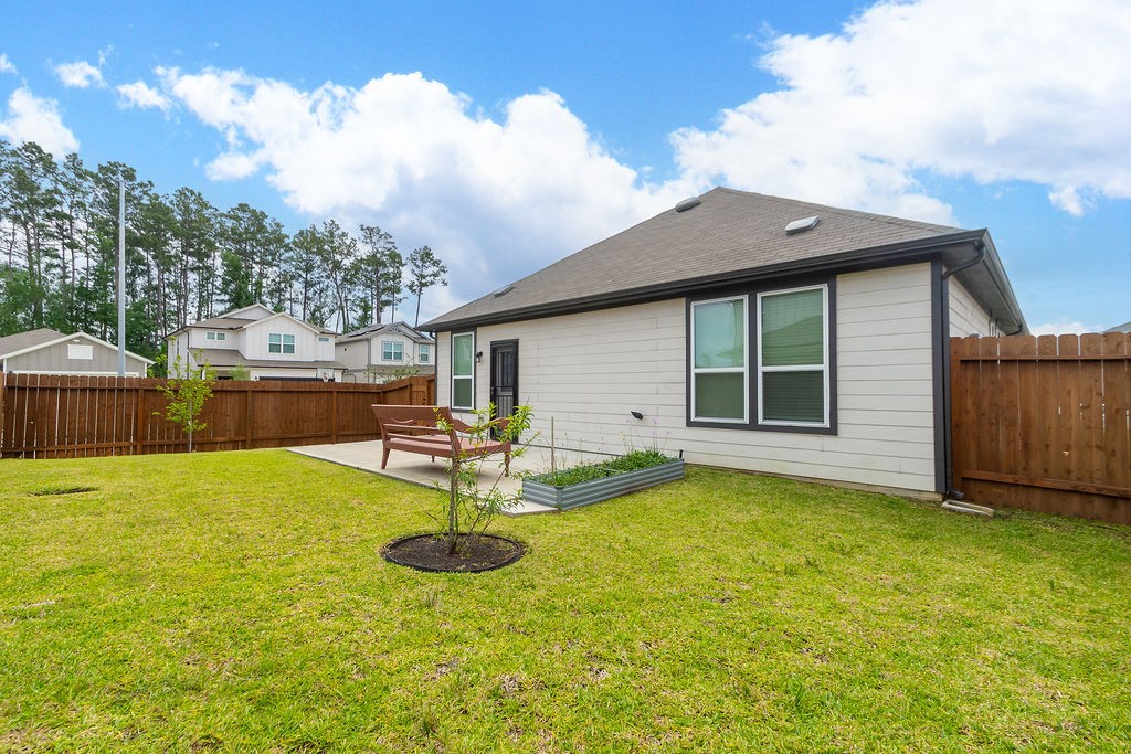 23502 Glenbuck St Spring Spring, TX 77373 - Photo 47 of 50 This photo features a well-maintained backyard with a grassy lawn, a wooden fence for privacy, and a small patio area with outdoor seating. The house has a modern exterior with large windows, and there's a small garden bed perfect for planting.