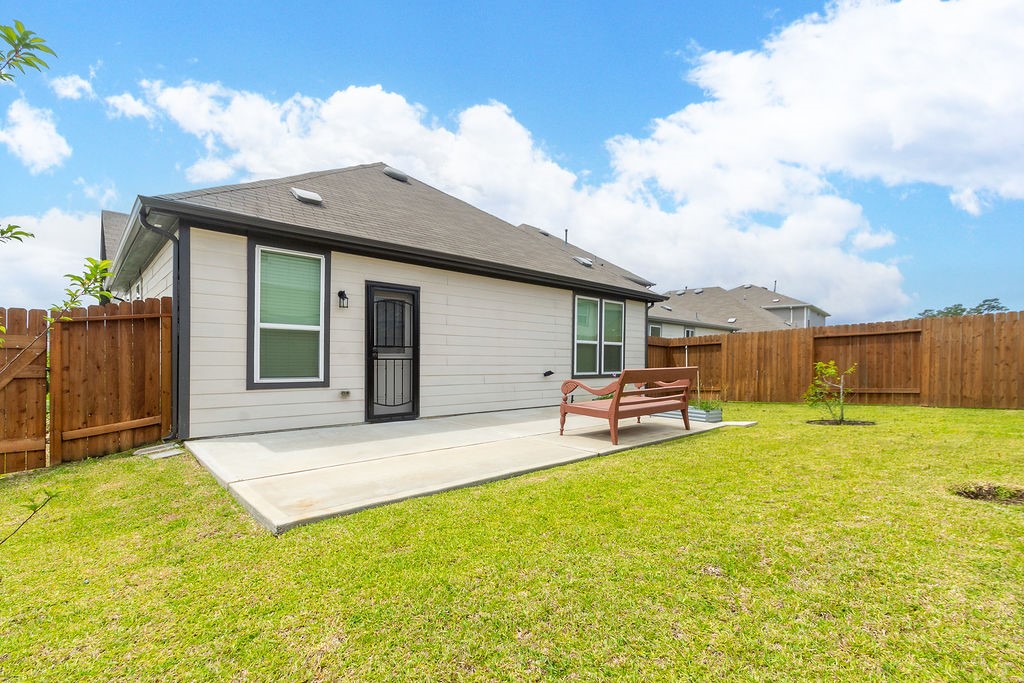 23502 Glenbuck St Spring Spring, TX 77373 - Photo 49 of 50 This photo shows a cozy backyard featuring a well-maintained lawn, a concrete patio area with a bench, and a wooden privacy fence. The house has a modern exterior with large windows, providing a bright and inviting outdoor space perfect for relaxation.