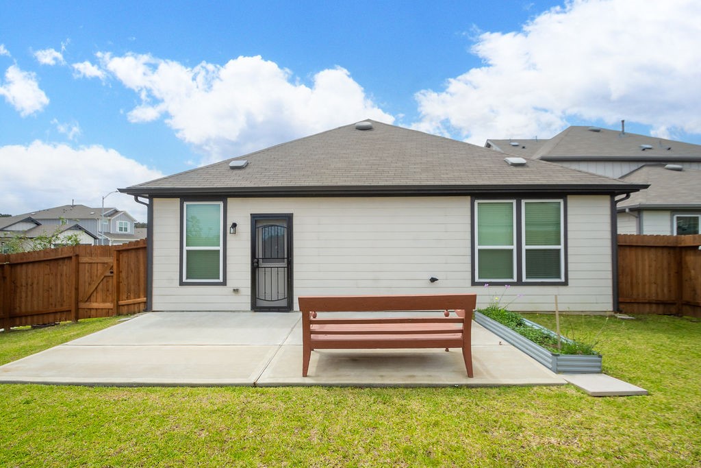 23502 Glenbuck St Spring Spring, TX 77373 - Photo 50 of 50 This photo showcases the backyard of a single-story home with a fenced yard. The house features a clean, modern exterior with large windows and a central door. There's a spacious concrete patio with a bench, perfect for outdoor relaxation.