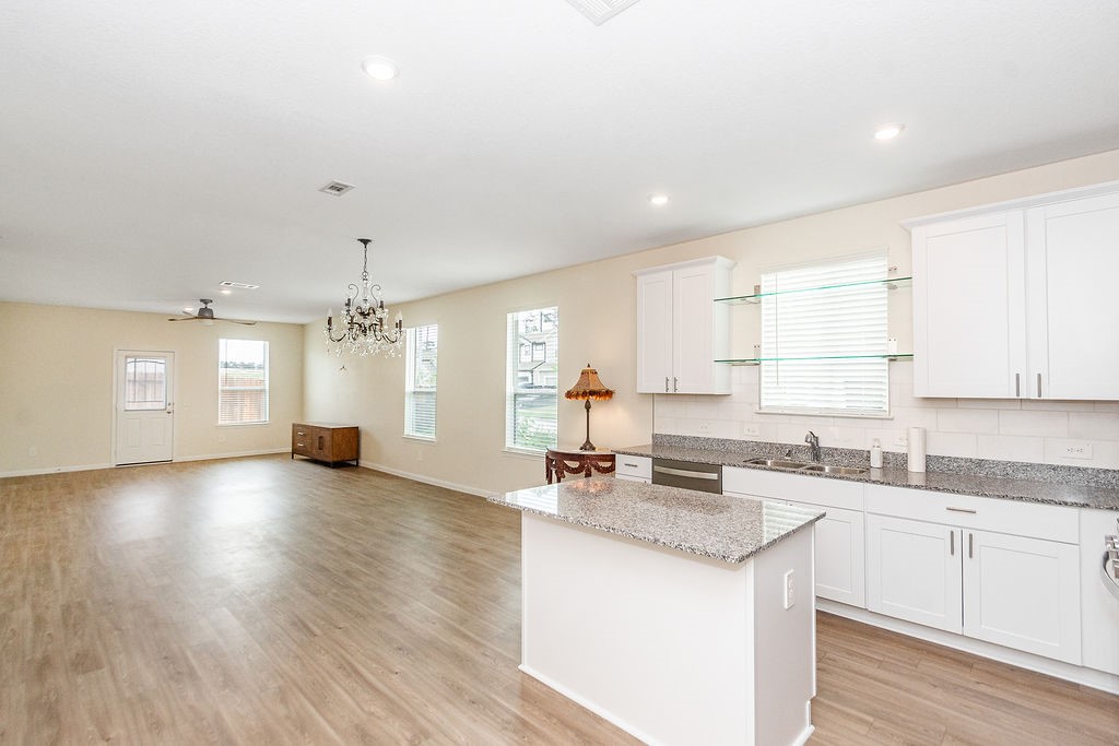 23502 Glenbuck St Spring Spring, TX 77373 - Photo 6 of 50 This photo showcases a spacious open-plan living area with wood-look flooring, featuring a modern kitchen with white cabinets and granite countertops. The room is well-lit with recessed lighting, a chandelier, and natural light from multiple windows.