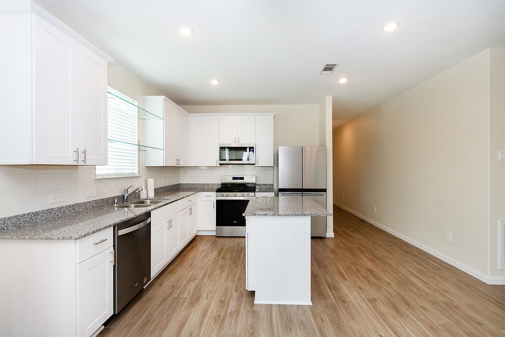 23502 Glenbuck St Spring Spring, TX 77373 - Photo 9 of 50 Modern kitchen with white cabinets, granite countertops, and stainless steel appliances. It features an open layout with wood flooring and ample natural light.