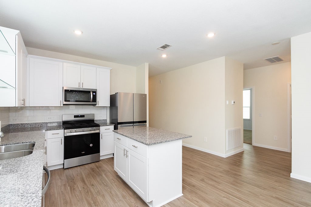 23502 Glenbuck St Spring Spring, TX 77373 - Photo 10 of 50 This modern kitchen features white cabinetry, granite countertops, and stainless steel appliances, including a built-in microwave and oven. The open layout and wood-style flooring enhance the bright, spacious feel.