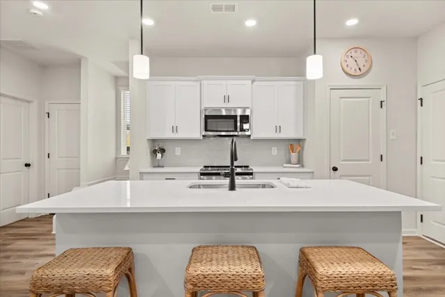 a kitchen with stainless steel appliances a stove a sink and white cabinets with wooden floor