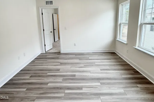 a view of an empty room with wooden floor and window
