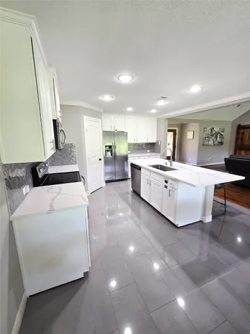 a large kitchen with stainless steel appliances a stove a refrigerator a sink dishwasher a dining table and chairs with wooden floor