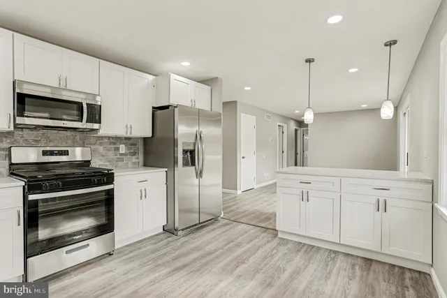 a kitchen with stainless steel appliances a stove a sink cabinets a refrigerator and a wooden floor