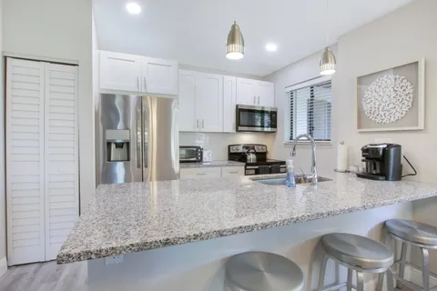 a kitchen with granite countertop a refrigerator a stove a sink a dining table and chairs