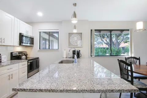 a kitchen with granite countertop a stove a sink a dining table and chairs