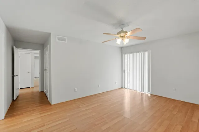 a view of an empty room with chandelier fan and wooden floor