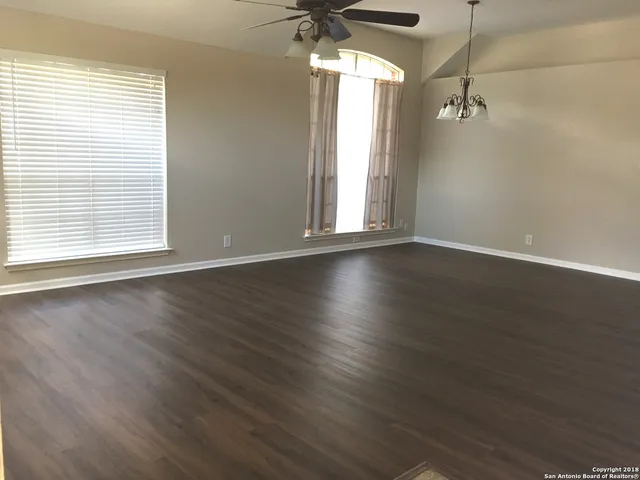 an empty room with wooden floor a ceiling fan and windows