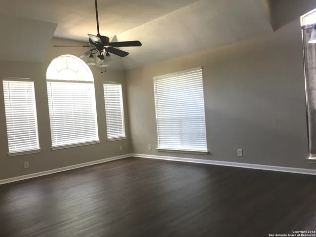 an empty room with wooden floor chandelier fan and windows