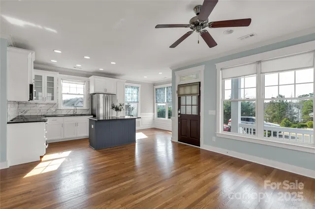 a kitchen with stainless steel appliances granite countertop a refrigerator a sink a stove and white cabinets with wooden floor next to windows