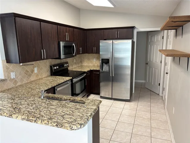 a kitchen with stainless steel appliances granite countertop a refrigerator a stove and a sink with wooden cabinets