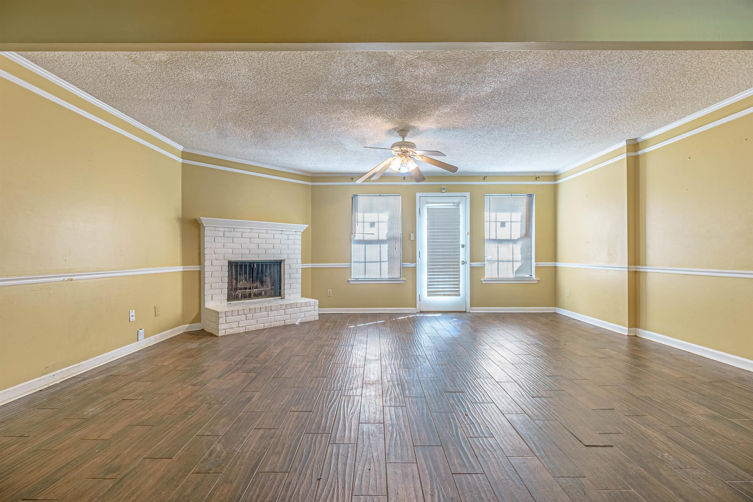 5891 Ridgehill Drive Memphis, TN 38141 - Photo 5 of 13 Unfurnished living room featuring ceiling fan, a textured ceiling, a brick fireplace, and dark hardwood / wood-style floors