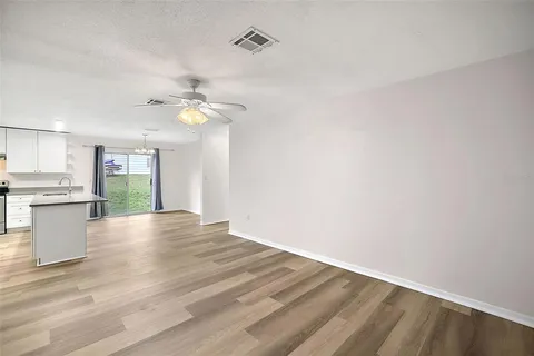 a view of an empty room with wooden floor and a kitchen