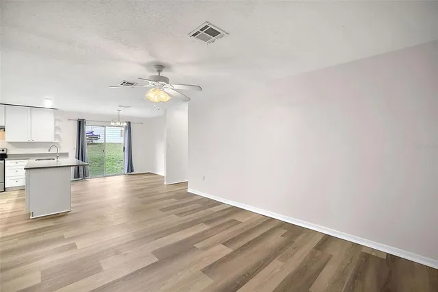 a view of an empty room with wooden floor and a kitchen