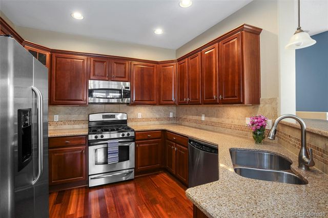 a kitchen with stainless steel appliances granite countertop a sink stove refrigerator and cabinets
