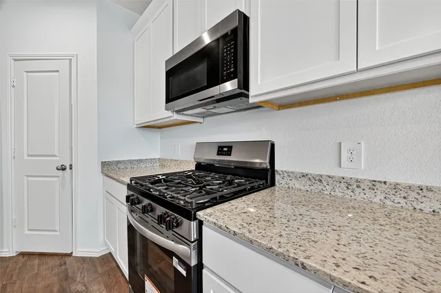 a kitchen with stainless steel appliances granite countertop white cabinets and a stove top oven