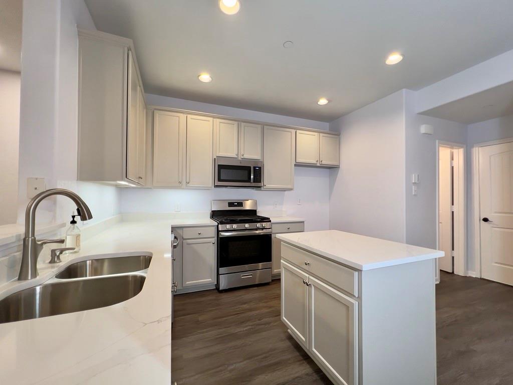 1902 Downing Street Allen, TX 75013 - Photo 7 of 19 Kitchen featuring stainless steel appliances, a center island, recessed lighting, light stone countertops, and dark wood-style flooring