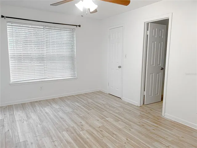 an empty room with wooden floor chandelier fan and windows