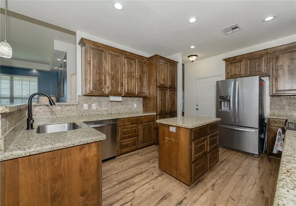 a kitchen with stainless steel appliances granite countertop a stove top oven a refrigerator a sink and dishwasher with wooden floor