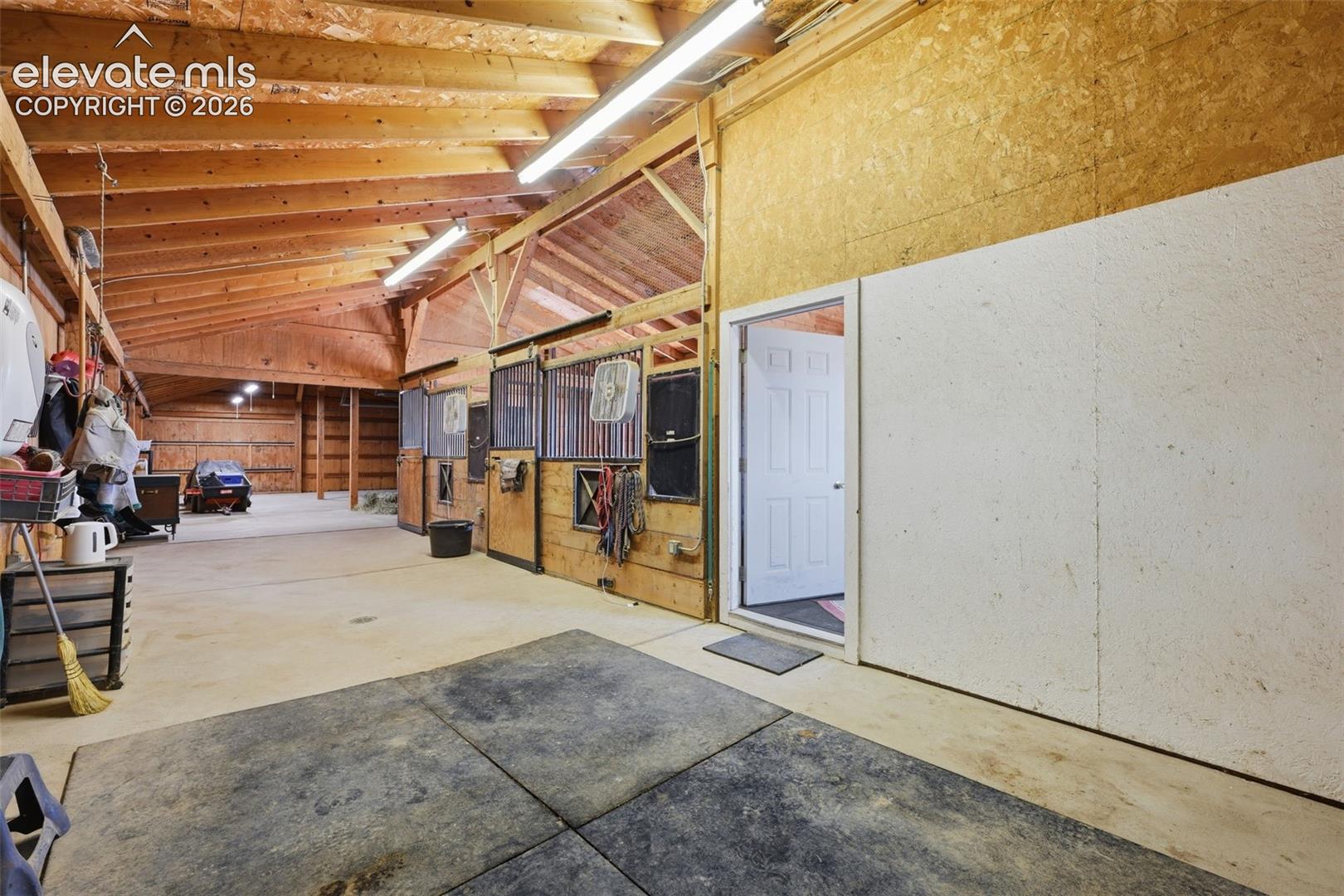 6015 West Condor Road Peyton, CO 80831 - Photo 40 of 50 Exposed wood-beam vaulted ceiling with fluorescent lighting, multiple stalls with metal grates, interior white panel door, and concrete flooring